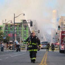 burning building with many fire trucks and one firefighter walking toward the camera.